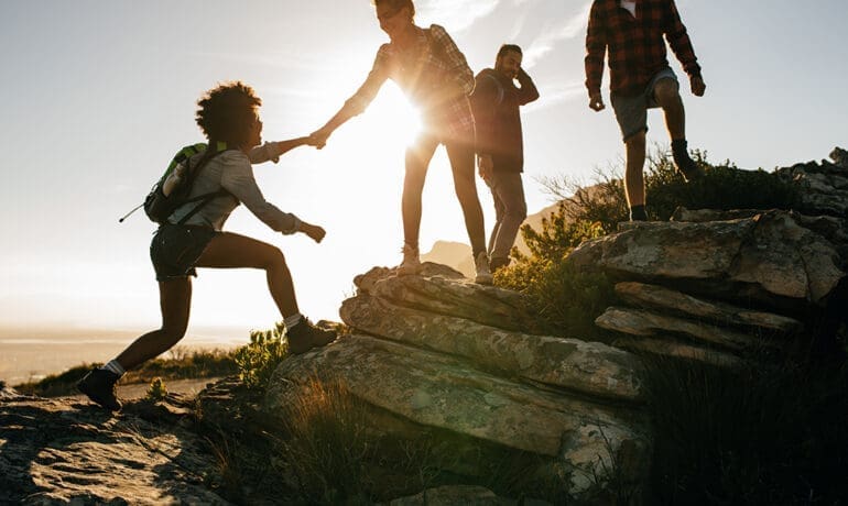 Group of people helping one another climb a rocky path, representing teamwork, focus, and shared direction.